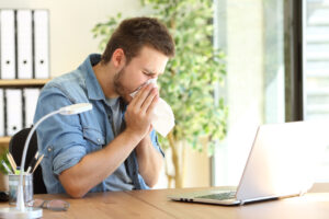 Man sneezing into a tissue from spring allergies while sitting in home