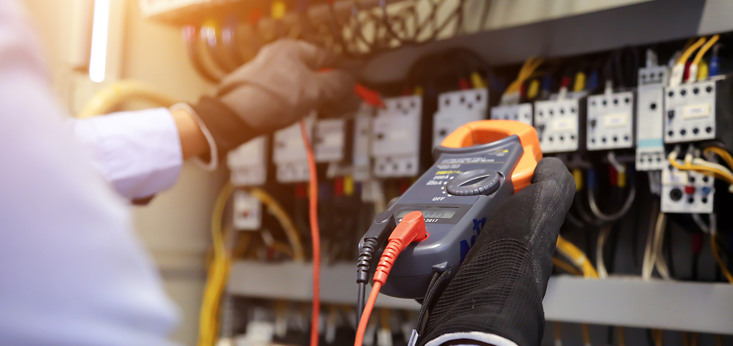 Electrician using digital multi-meter to check current voltage at circuit breaker in main distribution board.