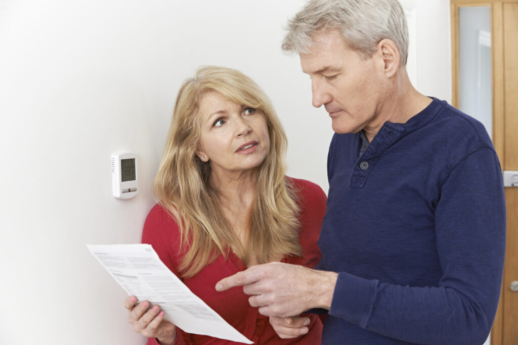 Concerned couple reviewing their energy bills while standing next to a thermostat